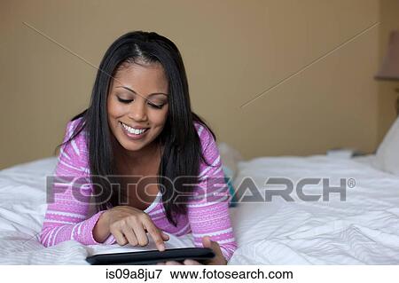 Young woman lying on bed using digital tablet View Large Photo Image Stock Photo - Young woman lying on bed using digital tablet. Fotosearch