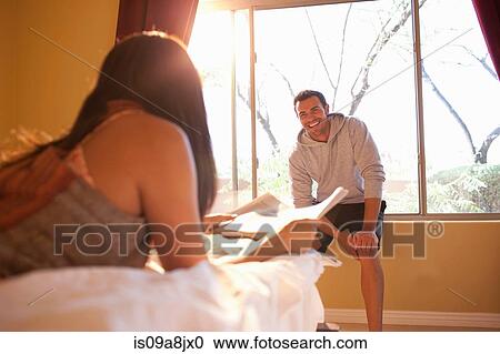 Young woman lying on bed with man sitting on window sill of hotel room View Large Photo Image Stock Image - Young woman lying on bed with man sitting on window sill of hotel room. Fotosearch