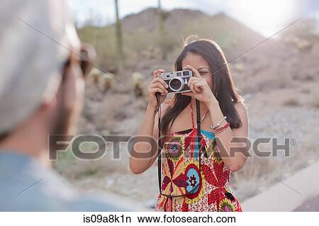 Picture - Young woman photographing boyfriend on desert road. Fotosearch