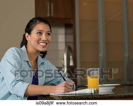 Young woman reading newspaper over orange juice, smiling View Large Photo Image Stock Image - Young woman reading newspaper over orange juice, smiling. Fotosearch