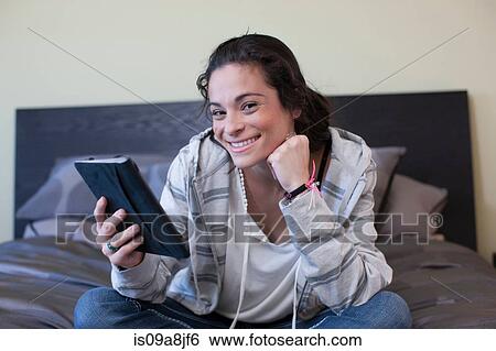 Stock Photograph - Young woman sitting bed reading electronic book, portrait. Fotosearch