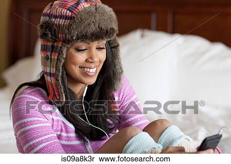 Young woman sitting on bed and listening to mp3 player, smiling View Large Photo Image Stock Photography - Young woman sitting on bed and listening to mp3 player, smiling. Fotosearch
