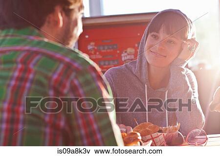 Stock Photo - Young woman smiling at man in sunlit diner. Fotosearch