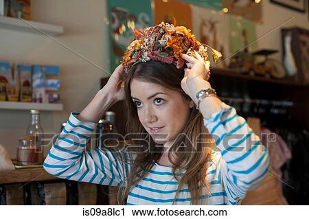 Stock Image - Young woman trying on floral hat in vintage shop. Fotosearch