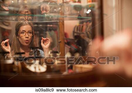 Stock Photo - Young woman trying on glasses and pulling faces in vintage shop. Fotosearch