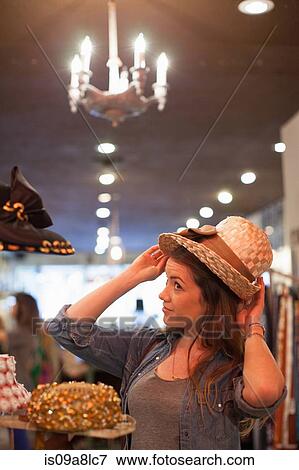 Stock Photo - Young woman trying on straw hat in vintage shop. Fotosearch