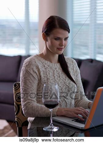 Stock Photography - Young woman using laptop with a glass of wine. Fotosearch
