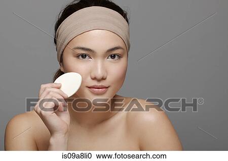 Stock Image - Young woman using make up sponge. Fotosearch
