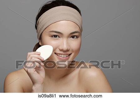 Stock Image - Young woman using make up sponge. Fotosearch