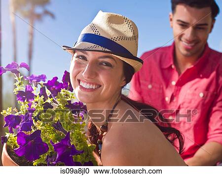 Stock Image - Young woman wearing sun hat and holding purple flowers, portrait. Fotosearch