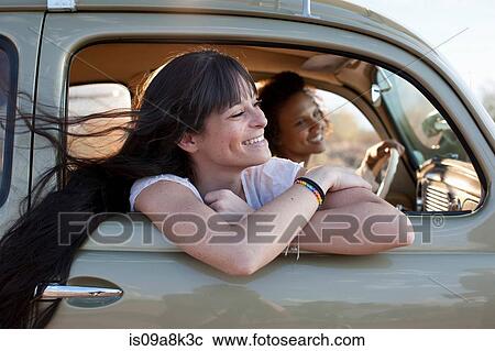 Stock Image - Young women travelling in car on road trip, smiling. Fotosearch