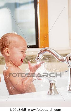 Stock Photo - Baby girl playing with water in tap. Fotosearch