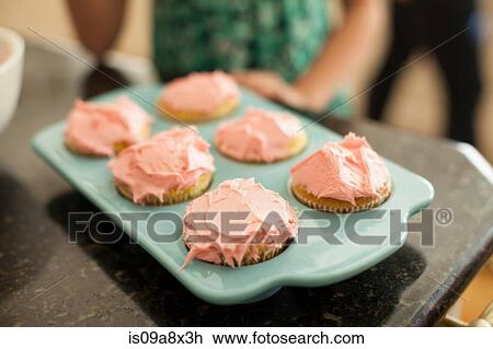 Stock Image - Baking tray with six iced cupcakes, close-up. Fotosearch