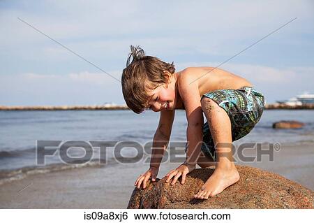 Boy crouching on rock on beach View Large Photo Image Stock Photograph - Boy crouching on rock on beach. Fotosearch