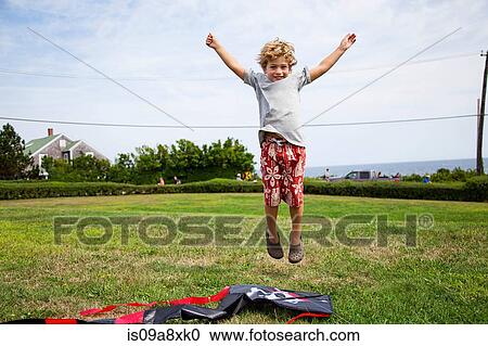 Stock Image - Boy jumping mid air in field. Fotosearch
