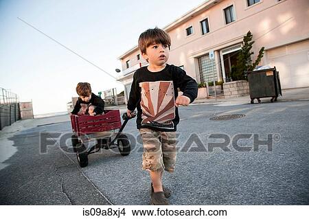 Picture - Boy pulling brother along in cart. Fotosearch