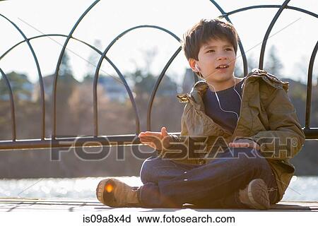 Stock Image - Boy sitting cross legged wearing earphones. Fotosearch