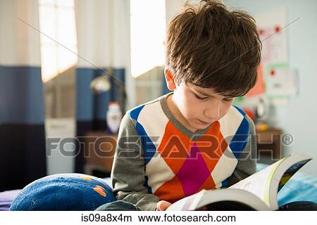 Picture - Boy sitting on bed reading book. Fotosearch