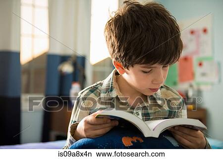 Picture - Boy sitting on bed reading book. Fotosearch
