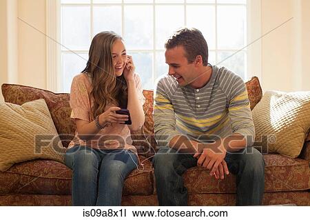 Stock Image - Brother and sister on sofa with earphones. Fotosearch