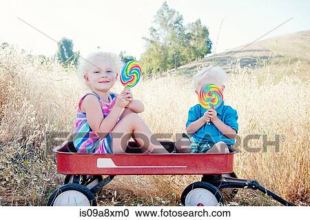 Stock Image - Brother and sister sitting in cart with lollipops. Fotosearch