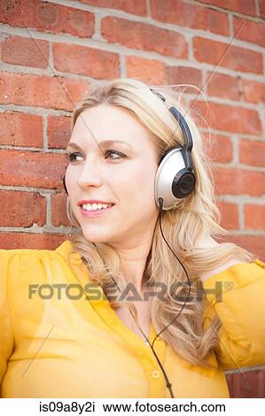 Stock Image - Close up of woman with headphones against brickwall. Fotosearch