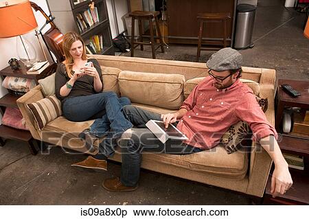 Couple sitting on sofa using digital tablet and smartphone View Large Photo Image Stock Photography - Couple sitting on sofa using digital tablet and smartphone. Fotosearch