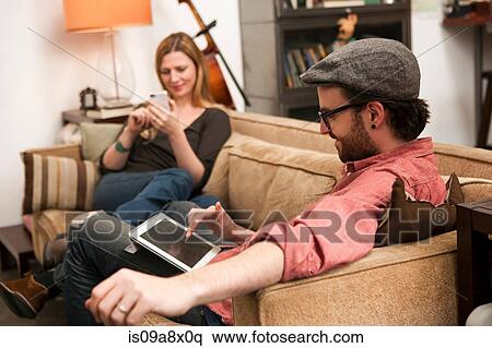 Couple sitting on sofa using digital tablet and smartphone View Large Photo Image Stock Photography - Couple sitting on sofa using digital tablet and smartphone. Fotosearch