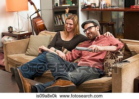 Stock Image - Couple sitting on sofa watching television. Fotosearch