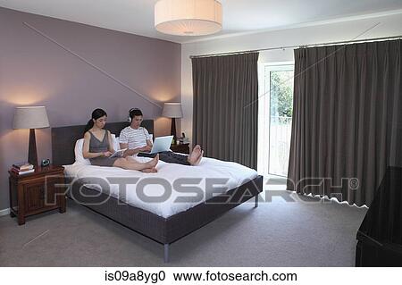 Stock Image - Couple surfing the internet in bedroom. Fotosearch