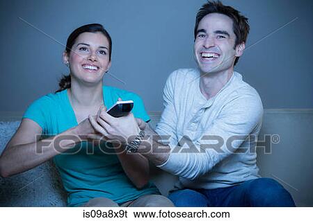 Stock Photograph - Couple watching television, fighting over remote control. Fotosearch