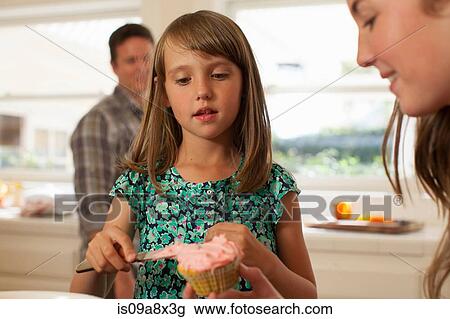 Stock Image - Daughter and mother icing cupcake. Fotosearch
