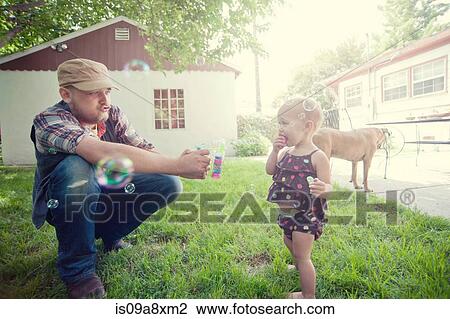 Stock Image - Father and baby daughter playing with bubbles in garden. Fotosearch