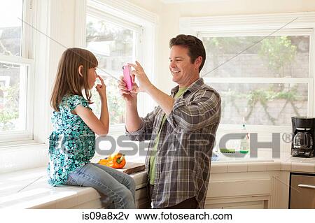 Stock Photo - Father photographing daughter on smartphone. Fotosearch