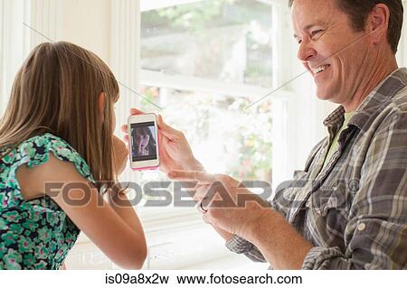 Father showing daughter photograph of her on smartphone View Large Photo Image Stock Photo - Father showing daughter photograph of her on smartphone. Fotosearch