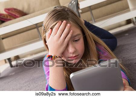 Stock Photograph - Girl looking at digital tablet in puzzlement. Fotosearch