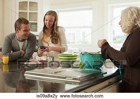 Stock Photo - Grandchildren with smartphone, grandmother preparing food. Fotosearch