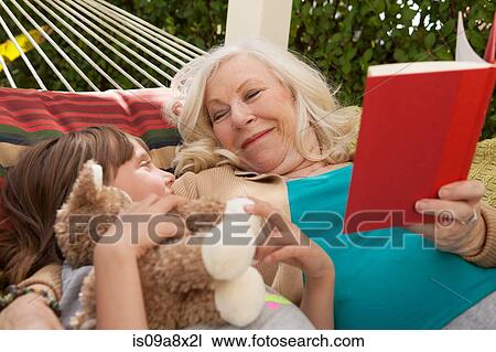 Stock Image - Grandmother and granddaughter reading book in hammock. Fotosearch