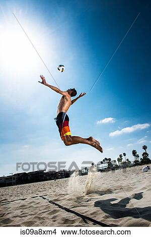 Picture - Male beach volleyball player jumping mid air to hit ball. Fotosearch
