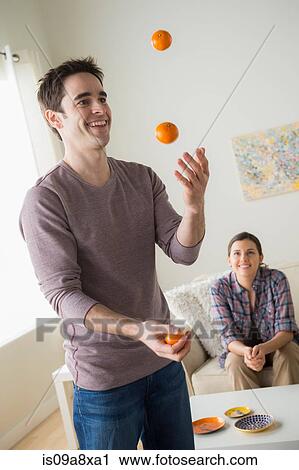 Stock Image - Man juggling oranges, woman watching. Fotosearch