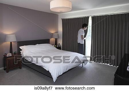 Stock Photo - Man peeping behind bedroom curtain. Fotosearch