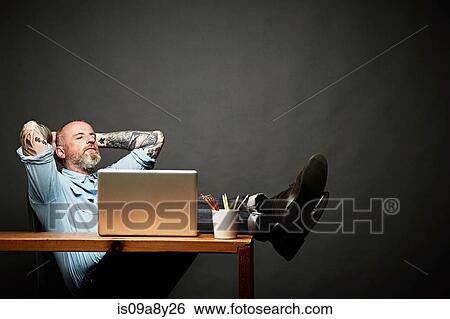 Man sitting back with legs on table View Large Photo Image Stock Photograph - Man sitting back with legs on table. Fotosearch