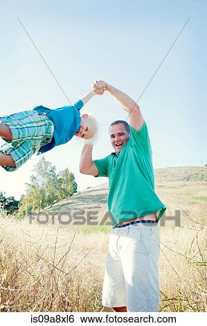 Stock Photograph - Man swinging son in field. Fotosearch