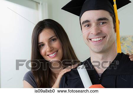 Stock Image - Man wearing mortarboard and graduation gown with woman. Fotosearch