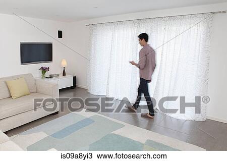 Stock Image - Man with mobile phone walking past curtains. Fotosearch