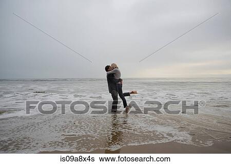 Stock Photograph - Mature couple embracing on beach. Fotosearch