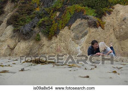 Picture - Mature couple lying on beach by rocks. Fotosearch