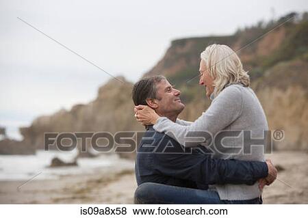 Stock Photo - Mature man lifting mature woman on beach. Fotosearch