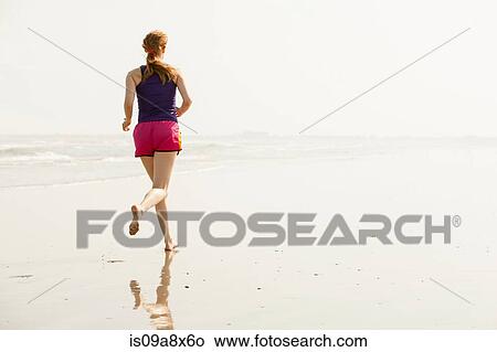 Picture - Mature woman jogging on beach. Fotosearch