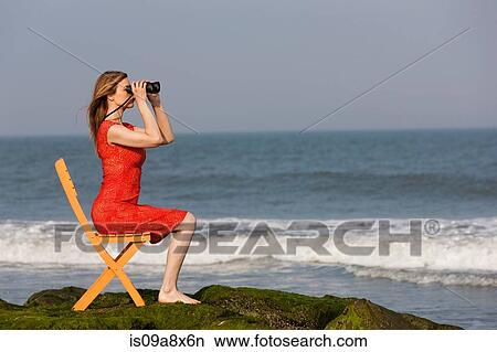 Mature woman sitting on chair on beach with binoculars View Large Photo Image Picture - Mature woman sitting on chair on beach with binoculars. Fotosearch